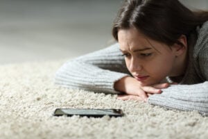 young woman on the floor looking anxiously at cell phone